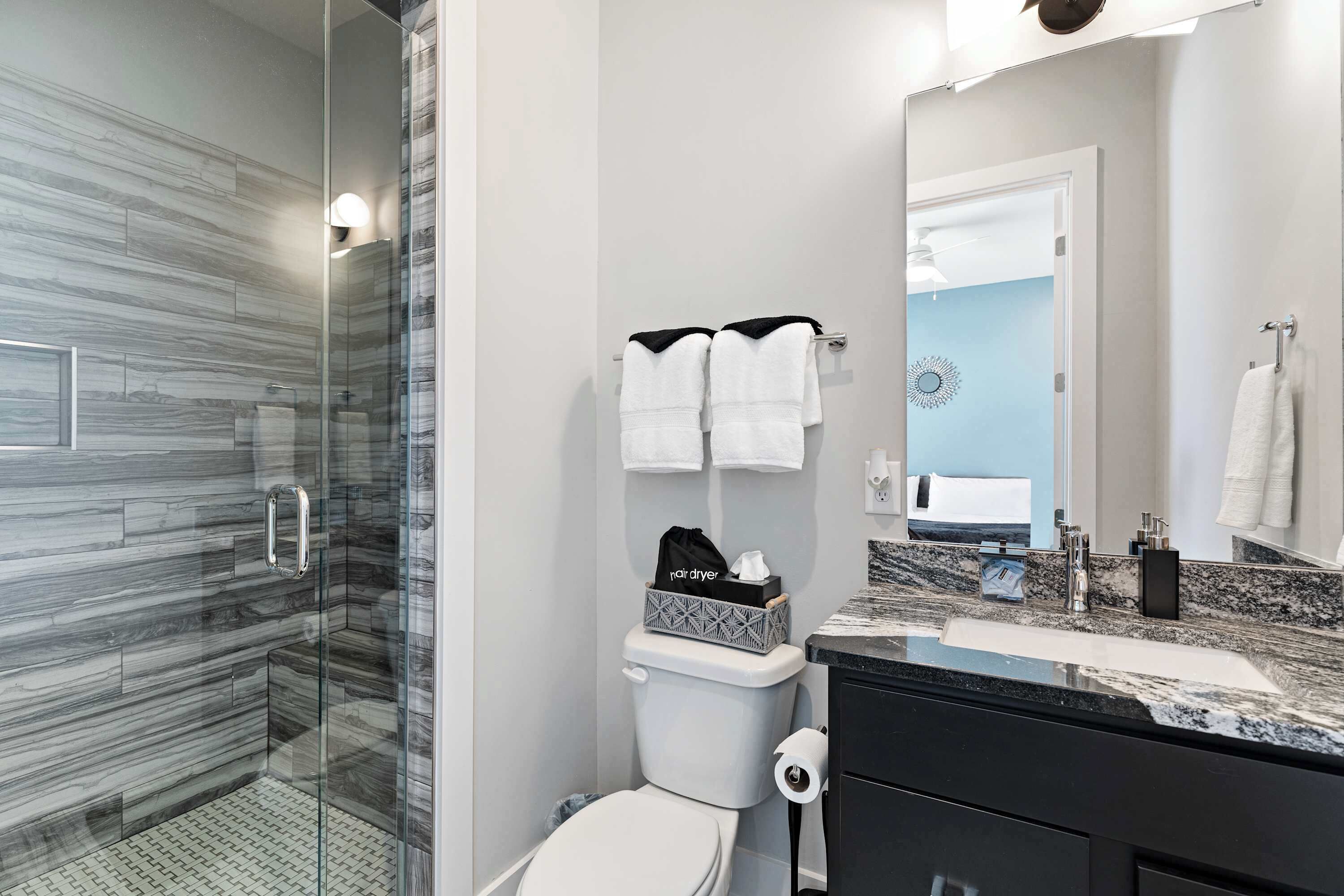 A modern bathroom with a glass shower enclosure, a toilet with a black bag on the tank, and a vanity with a mirror.
