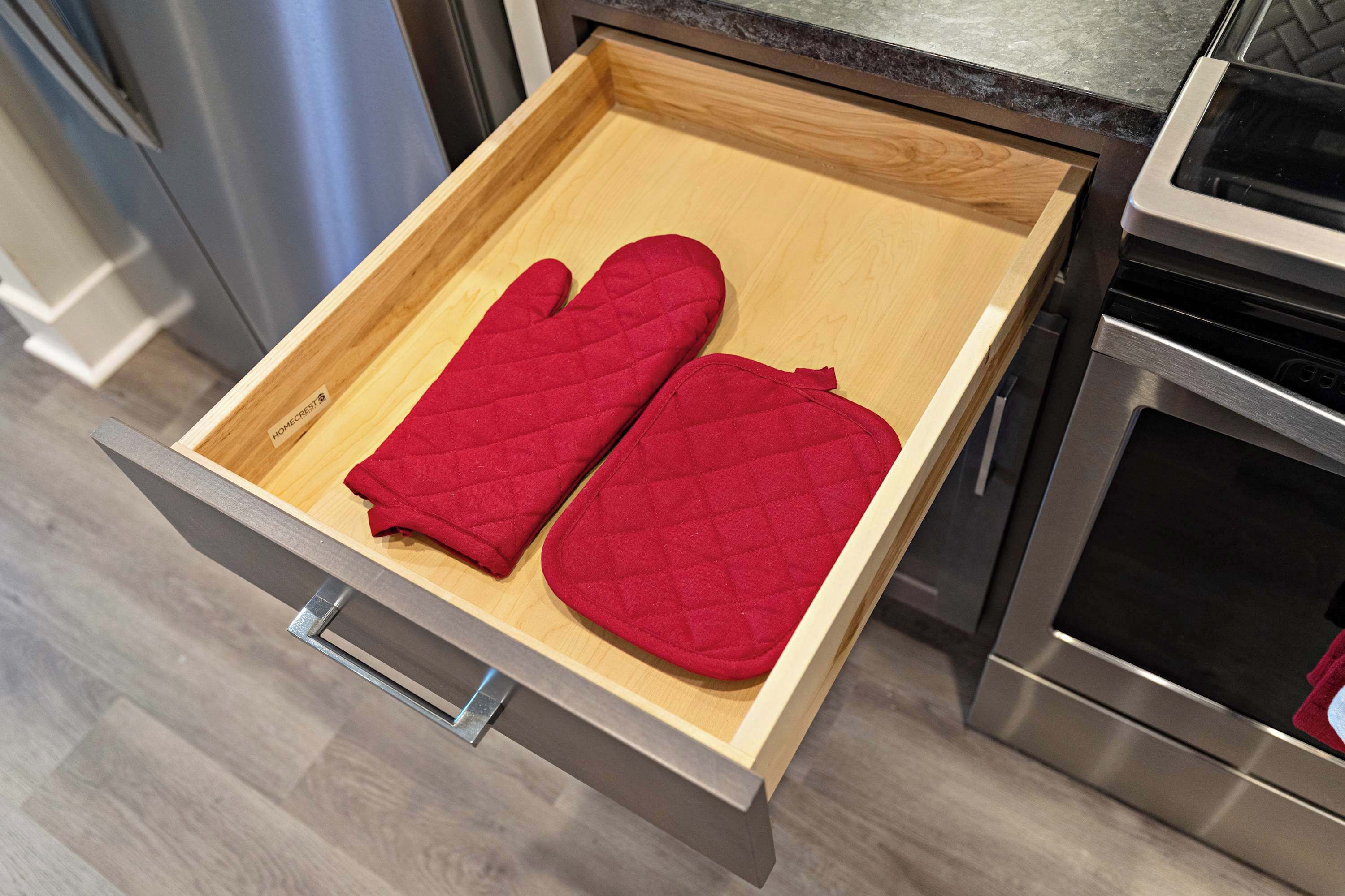 A kitchen drawer with two red oven mitts.