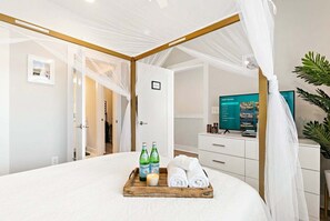 Een slaapkamer met een hemelbed, een nachtkastje met flessen en handdoeken, een televisie en een plant.