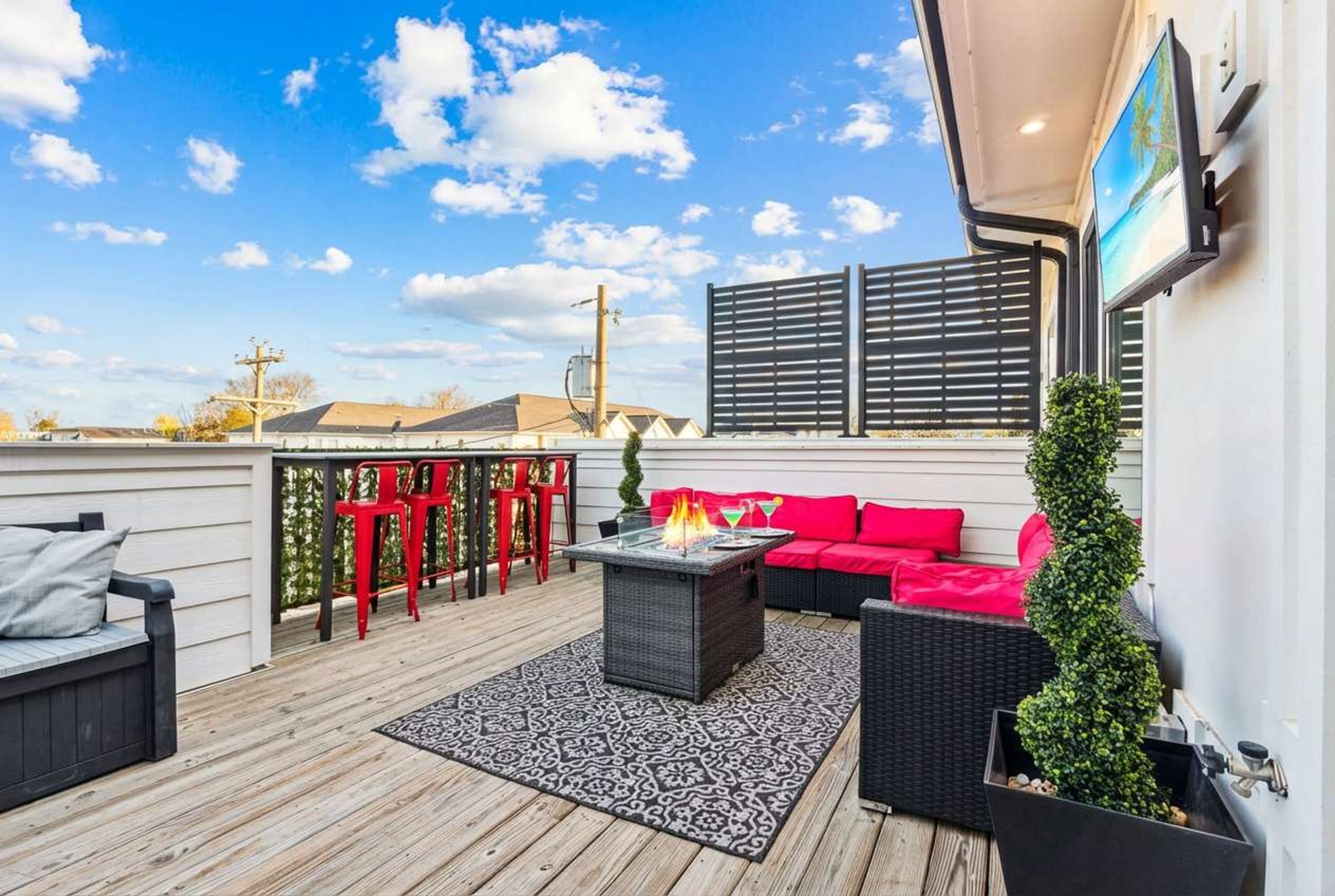 A covered outdoor patio with a fire pit, red and black furniture, and a view of the sky.