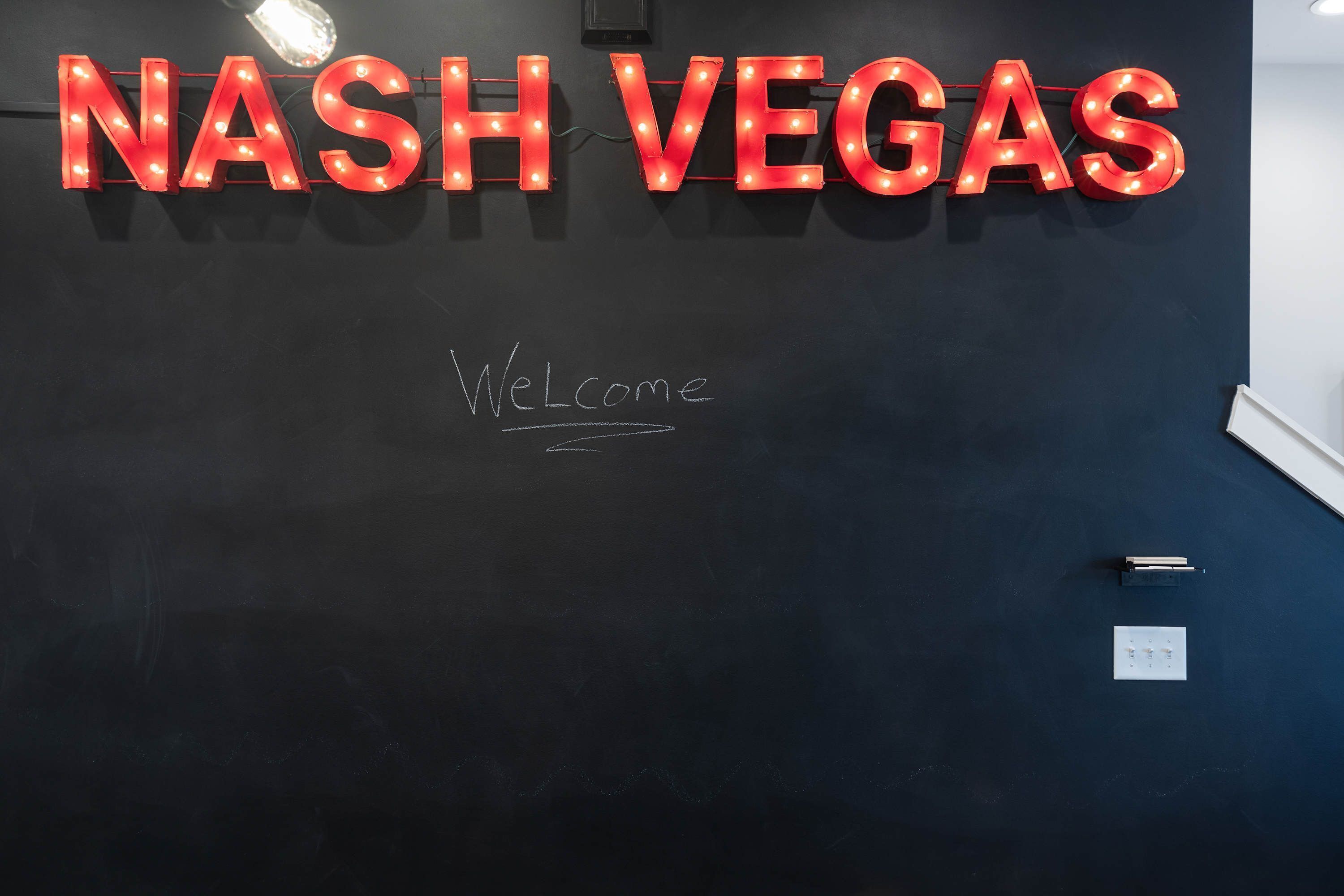Una pizarra con 'NASH VEGAS' en letras rojas y la palabra 'Bienvenido' escrita debajo.