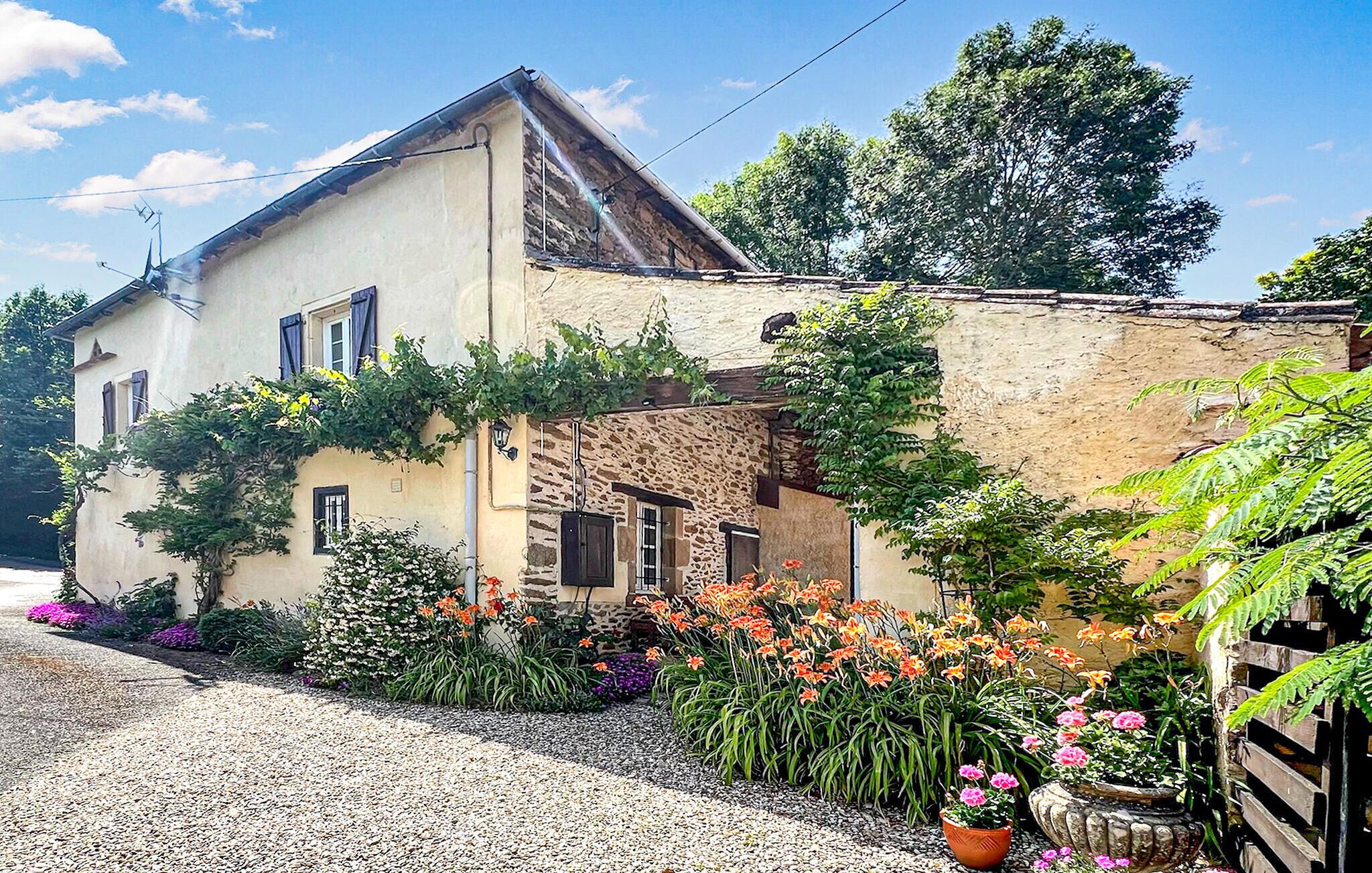 Una casa de dos pisos con fachada de piedra, camino de entrada de grava y diversas plantas florecientes.