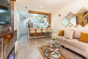 Un salon moderne avec un canapé, une table basse en verre et un coin repas comprenant des chaises, avec une cuisine en arrière-plan.