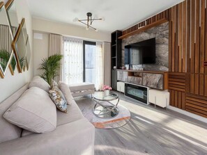A modern living room with a sofa, a round glass coffee table, a fireplace, and a flat-screen TV mounted on a wooden wall. - Luxury apartment with a pool, ocean view, air conditioning, and a digital fireplace (Lima)
