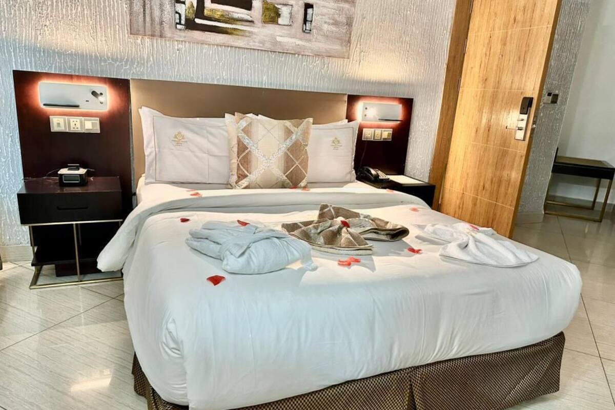 A hotel room with a large bed, a bedside table with a phone, a nightstand, and a wall-mounted light fixture.