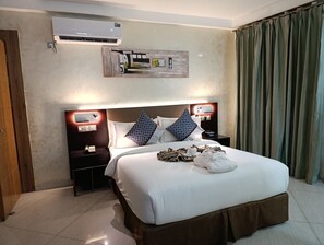 Camera d'albergo con un letto grande, due comodini, un condizionatore d'aria, un'opera d'arte appesa al muro e una tenda.