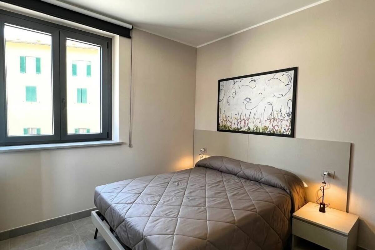 A modern bedroom with a bed, bedside tables, a ceiling light, a window, and a wall-mounted artwork.