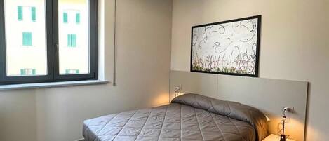 Ein modernes Schlafzimmer mit Bett, Nachttischen, einer Deckenleuchte, einem Fenster und einem Wandbild.