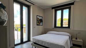 Une chambre à coucher comprenant un lit, une table de chevet, une lampe fixée au mur, une fenêtre avec vue et un luminaire au plafond.