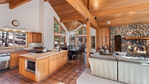 A spacious kitchen with wooden cabinets, a large island, and a stone fireplace. - Northstar Summer Hub | Hot Tub | MTB & Golf Access (Placer County)