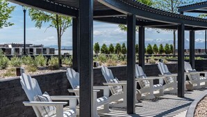 A covered outdoor seating area with white chairs and a pergola structure. - Views! Amenities! Pool/Spa/Gym/Bowl/Pking! (Salt Lake City)