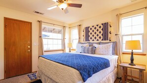 Une chambre à coucher avec un grand lit, un ventilateur de plafond, une fenêtre avec des rideaux et une table de chevet avec une lampe.