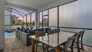 A sunlit patio with a dining table, chairs, and a seating area with cushions. - Gated 7BR Resort Villa w/ Private Heated & Lighted Pool | Corner Lot Near Disney (Kissimmee)