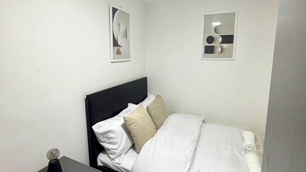A small, neatly arranged bedroom with a bed, bedside table, and a dresser. There are two wall-mounted mirrors and a ceiling light. - Lovely apartment in Preston perfect for your next getaway (Preston)