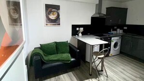 Eine kompakte Küche mit Essbereich, einer Waschmaschine und einem Sofa mit grüner Decke.