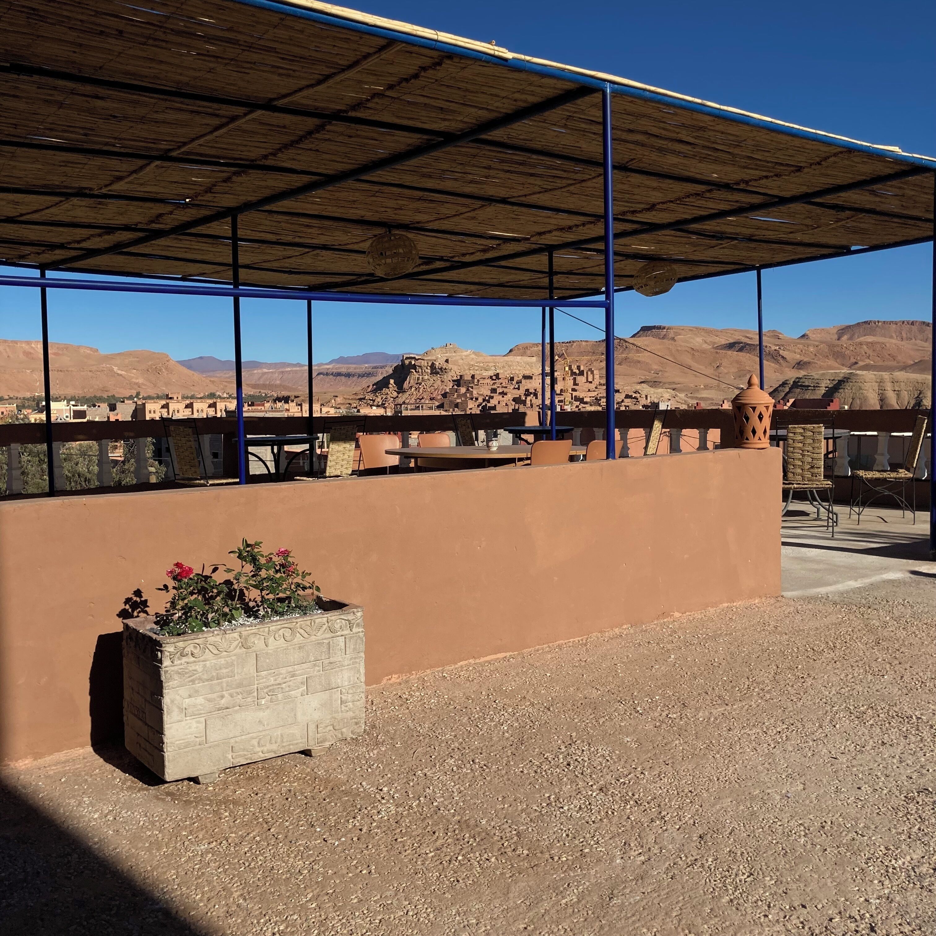 Un espace extérieur aménagé avec des sièges, offrant une vue sur un paysage désertique, notamment des montagnes et un petit village.