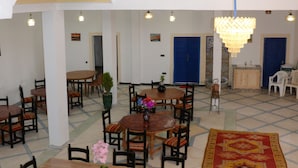 A spacious dining area with multiple tables and chairs, a chandelier, and a patterned carpet. - La Belle Vue Guest House  (Aït Benhaddou)