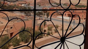 A view through a window with a decorative metal frame, featuring a desert landscape with buildings and a clear sky. - La Belle Vue Guest House  (Aït Benhaddou)