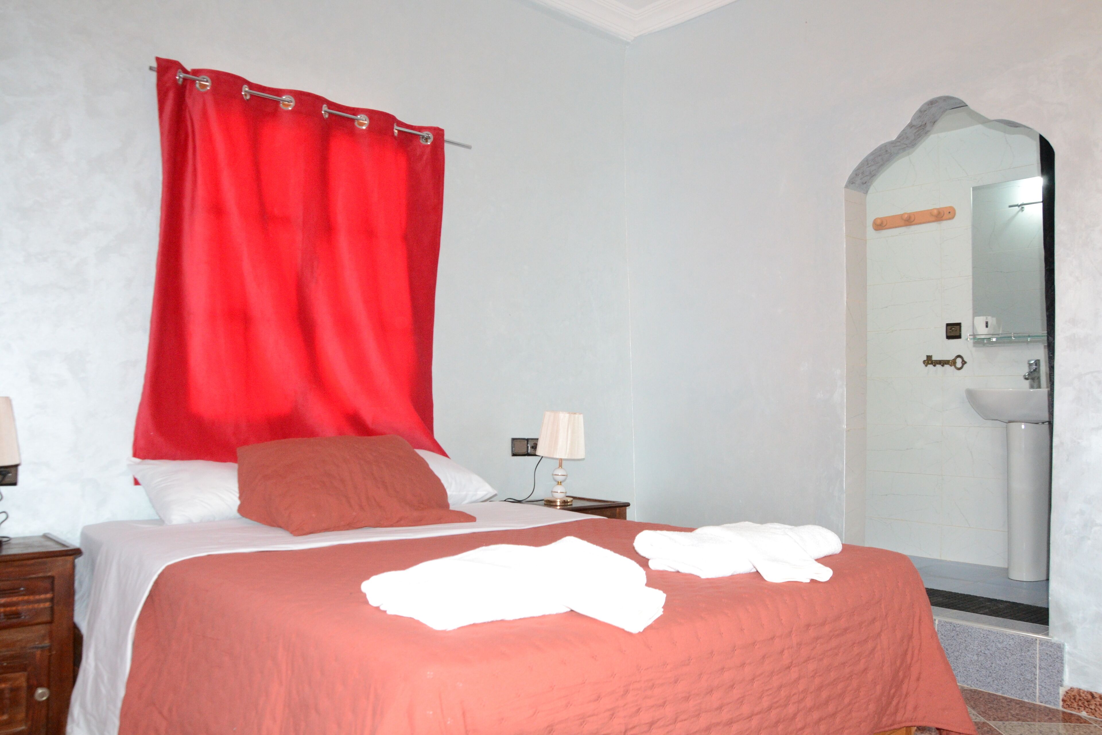 A hotel room with a bed, a nightstand, a lamp, a mirror, and a bathroom with a sink.