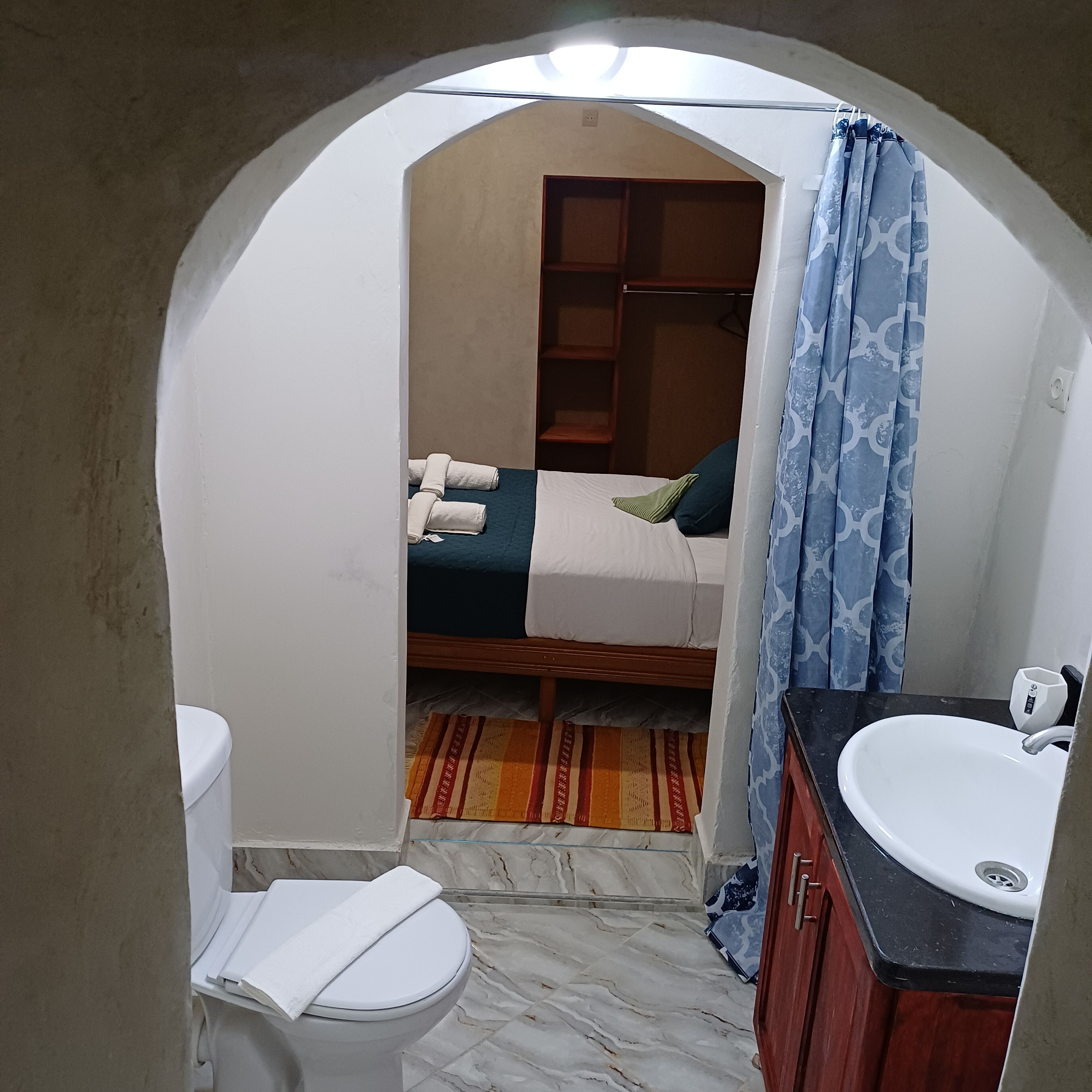 A small, compact room with a bed, a white toilet, a sink, and a shower area.