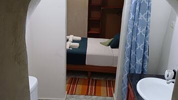 A small, compact room with a bed, a white toilet, a sink, and a shower area.