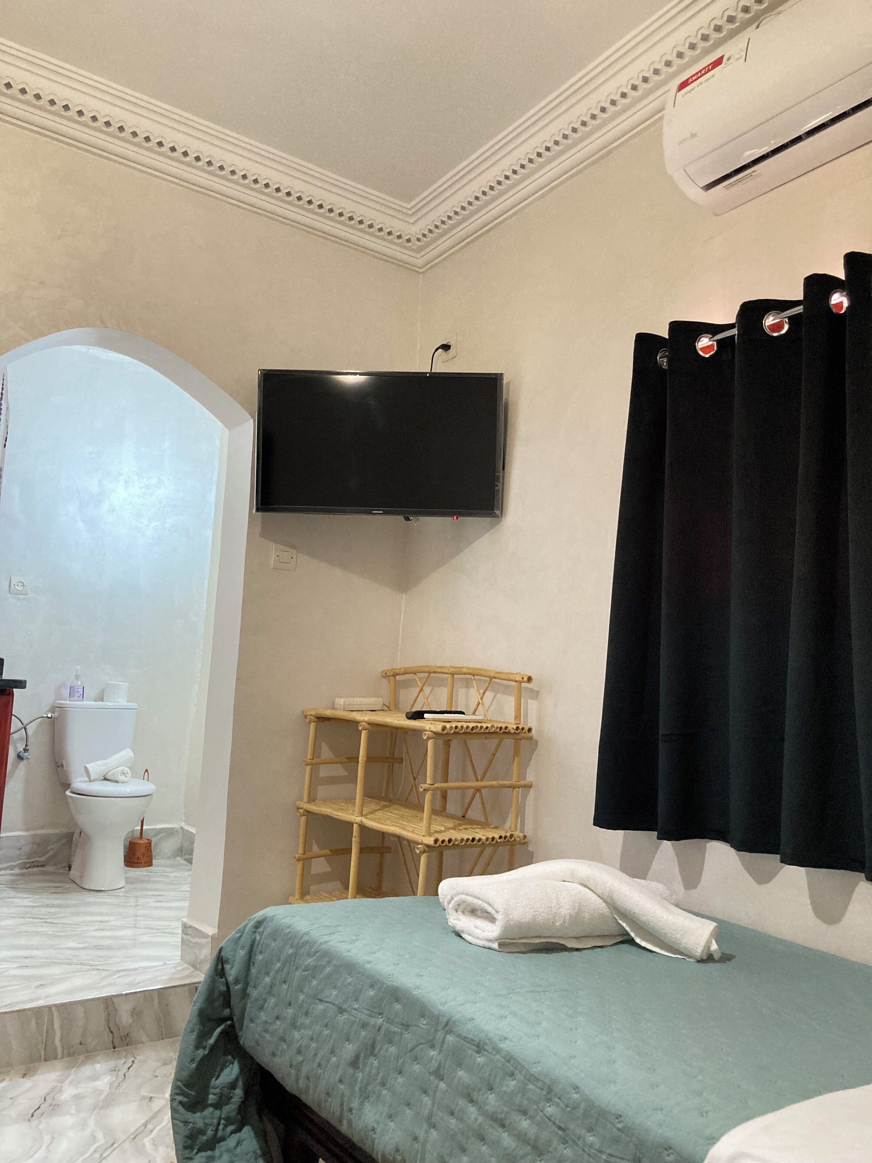 Habitación de hotel con cama, televisor montado en la pared, inodoro y zona de ducha.