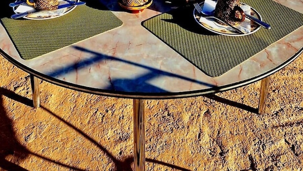 A table set with traditional Moroccan dishes, a pitcher, and glasses of orange juice on a balcony overlooking a mountainous village. - La Belle Vue Guest House  (Aït Benhaddou)
