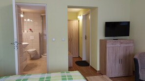 Ein Hotelzimmer mit Bett, Fernseher, Kleiderschrank, Bad mit Toilette und Dusche sowie einem kleinen Flur.
