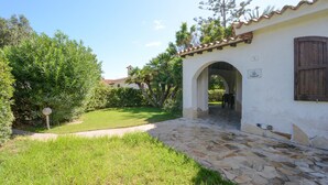 A stone pathway leading to a white building with a tiled roof and an archway entrance. - 3 bedroom awesome home in Costa Rei (Costa Rei)