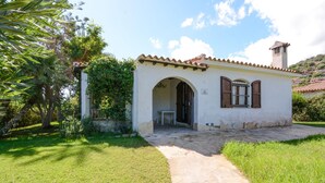 A small, single-story building with a tiled roof, an arched entrance, and a window with wooden shutters. - 3 bedroom awesome home in Costa Rei (Costa Rei)