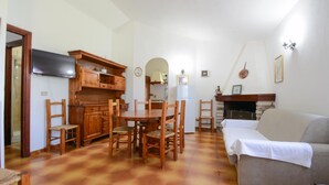 A cozy living room with a fireplace, a dining area with wooden furniture, and a kitchen with a built-in stove. - 3 bedroom awesome home in Costa Rei (Costa Rei)
