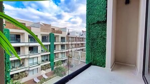 Un balcón con vistas a un complejo moderno de edificios, un muro verde y un cielo despejado.