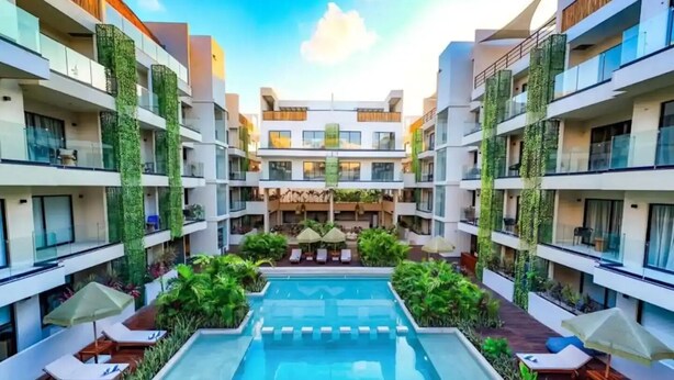 Un hotel moderno con una piscina central rodeada de zonas de descanso y vegetación.
