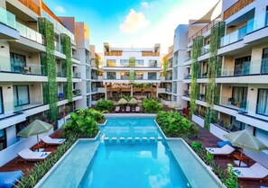 A modern hotel with a central swimming pool surrounded by lounge areas and greenery. - Luxury PH Studio - 5 Star Resort-Style Escape (Tulum)