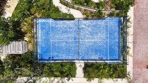 Oversigtsbillede af en tennisbane omgivet af frodig vegetation og en belagt sti.