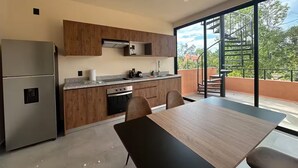 Et moderne køkken med træskabe, stålstål-hvidevarer og et spiseområde med et stort vindue med udsigt til en balkon.