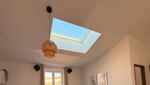A compact living space with a skylight, a round dining table, a sofa with cushions, and a small kitchen area. - Joli t2 (Marius) (Aubagne)