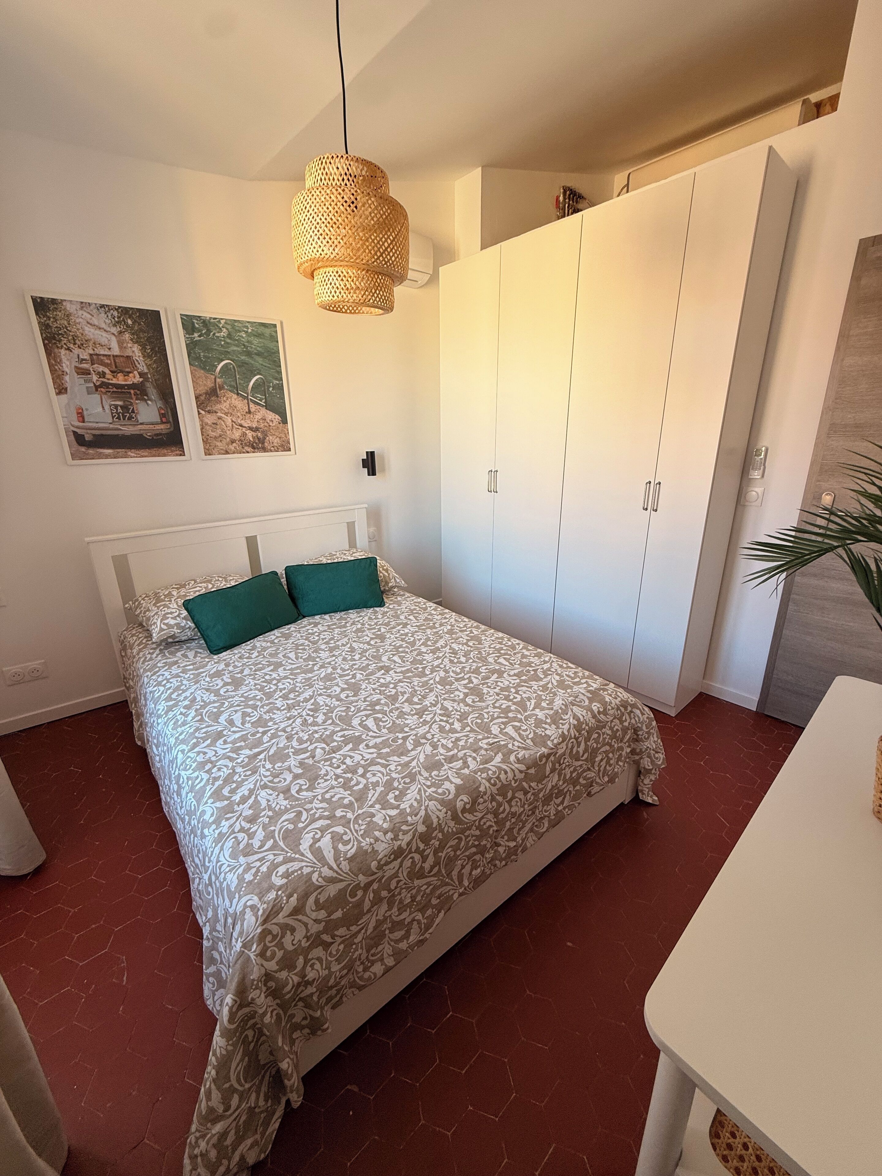 A bedroom with a bed, a wardrobe, a hanging light fixture, and two wall-mounted pictures.