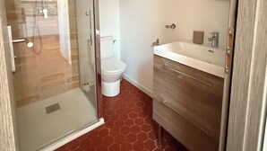 A bathroom with a glass shower enclosure, a toilet, a sink with a mirror, and a wooden vanity. - Joli t2 (Marius) (Aubagne)