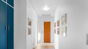 Un passadís amb sòl de fusta, parets blanques i una porta de fusta al final.