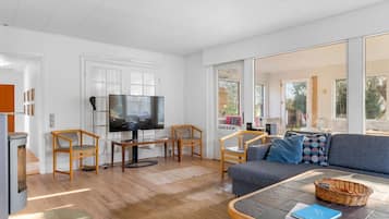 Uma sala de estar moderna com televisão de tela plana, móveis de madeira e grandes janelas.
