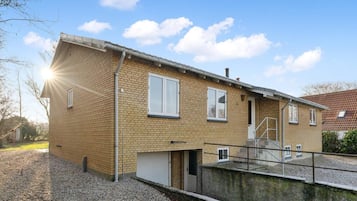 Um edifício residencial de dois andares com fachada de tijolo, garagem e uma pequena área externa com cascalho.