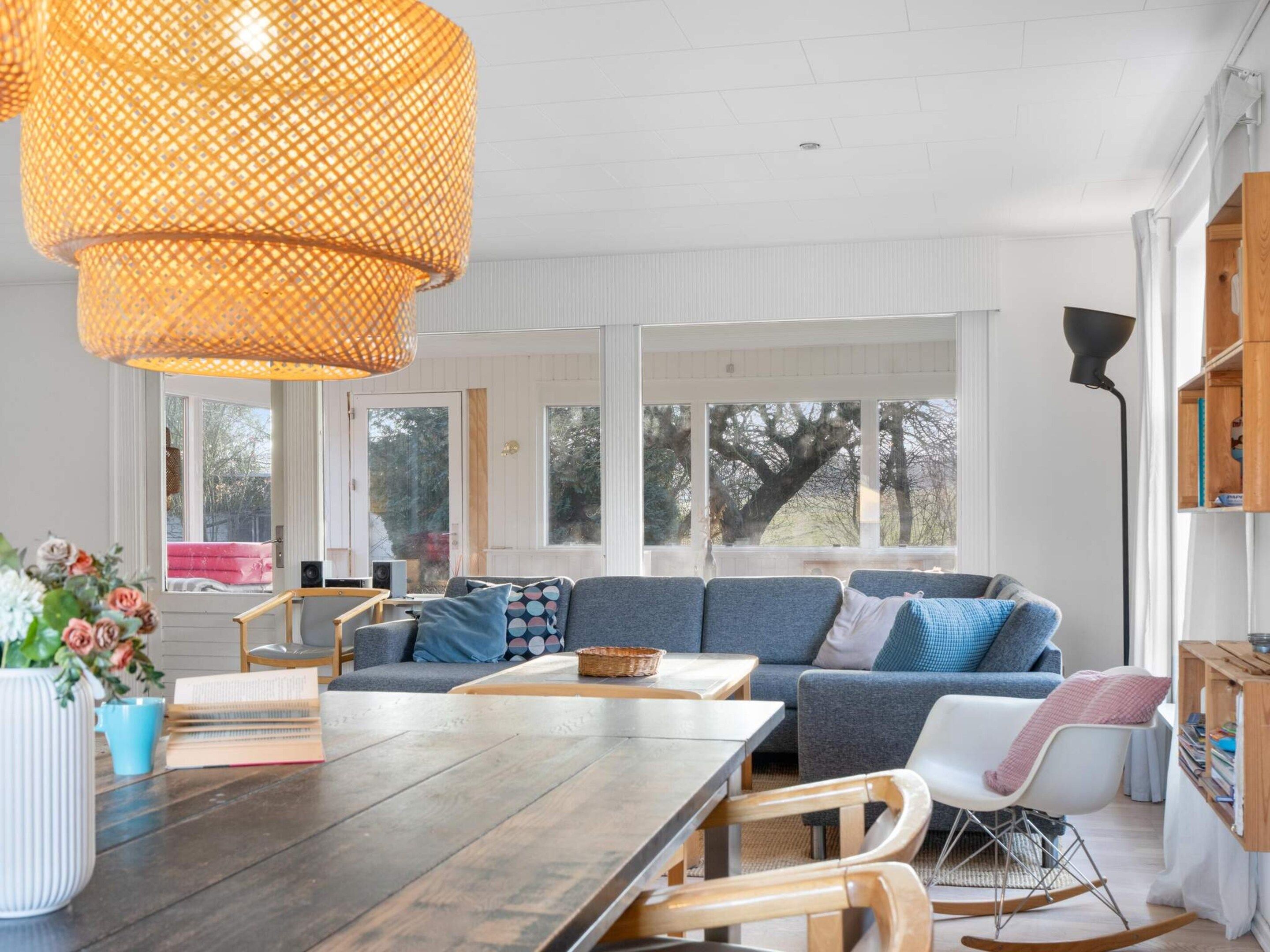 Una sala moderna con una mesa de comedor de madera, un sofá azul y un amplio ventanal que proporciona luz natural.