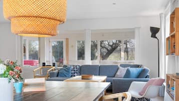 Sala de estar moderna com mesa de jantar de madeira, sofá azul e uma grande janela que ilumina naturalmente o espaço.