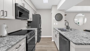 A modern kitchen with a built-in oven, microwave, and dishwasher. There is a large round mirror on the wall and a clock. - Resort Stay~Near Disney~Bright~Gym~Hot Tub (Kissimmee)