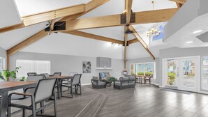 A spacious loft-style room with a high ceiling, exposed wooden beams, a dining area with a long table and chairs, a seating area with sofas, and large windows offering views of the outside. - Resort Stay~Near Disney~Bright~Gym~Hot Tub (Kissimmee)