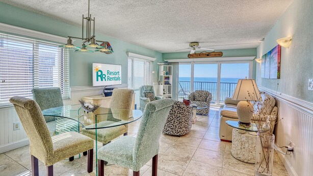 A spacious living room with a glass coffee table, patterned chairs, a sofa, and a view of the ocean. - Ocean Sands 1-501 (Madeira Beach)