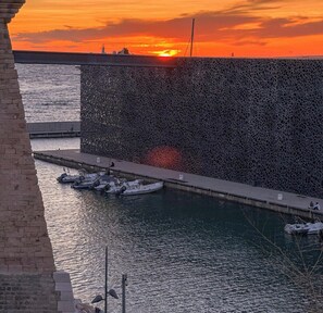 Udsigt over vandet i solnedgang, med både i havnen og en stor mur.