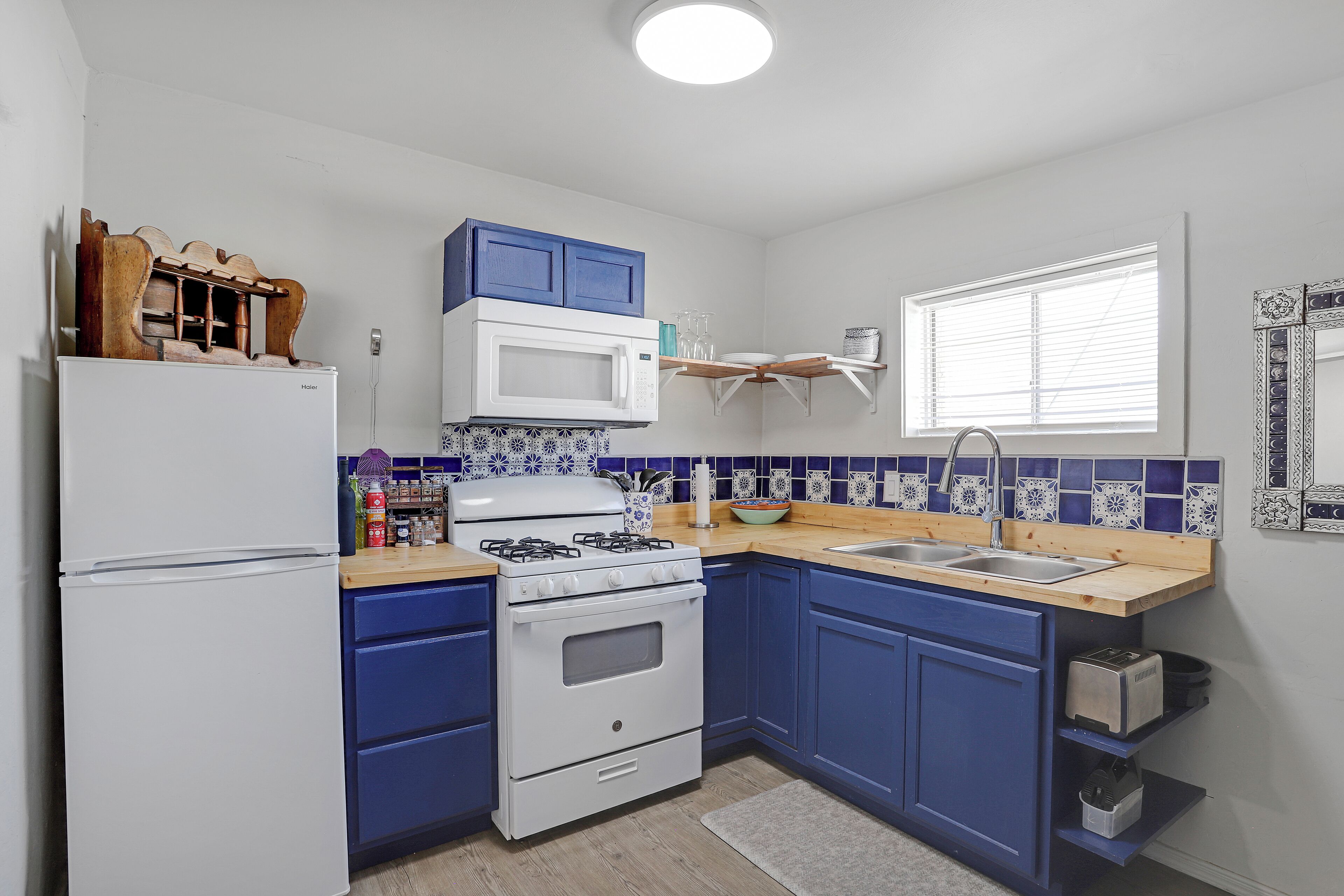 A compact kitchen with a white refrigerator, a stove, and a microwave. There are blue cabinets and a wooden countertop.