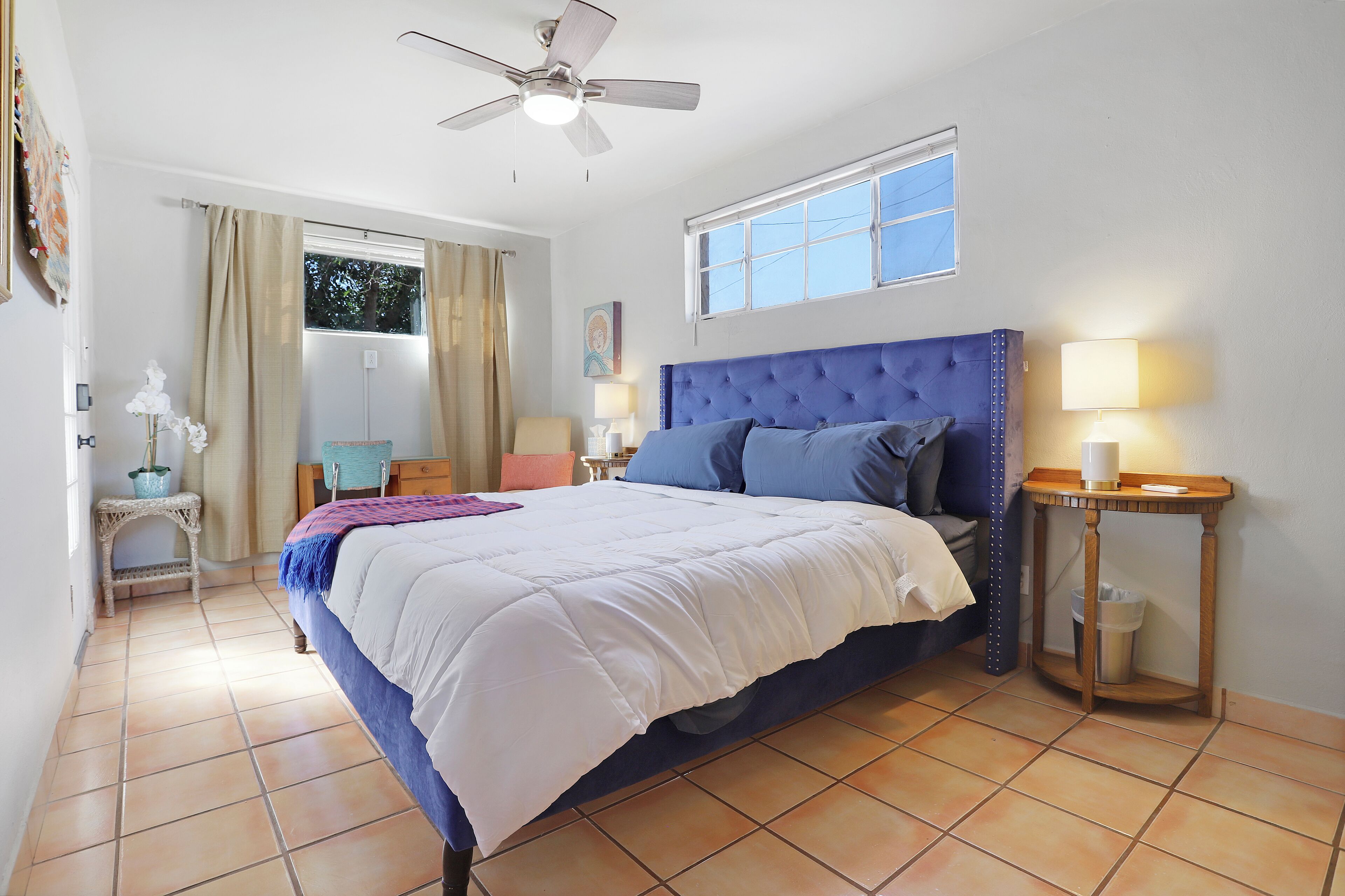 A bedroom with a bed, a ceiling fan, a window, and a nightstand with a lamp.
